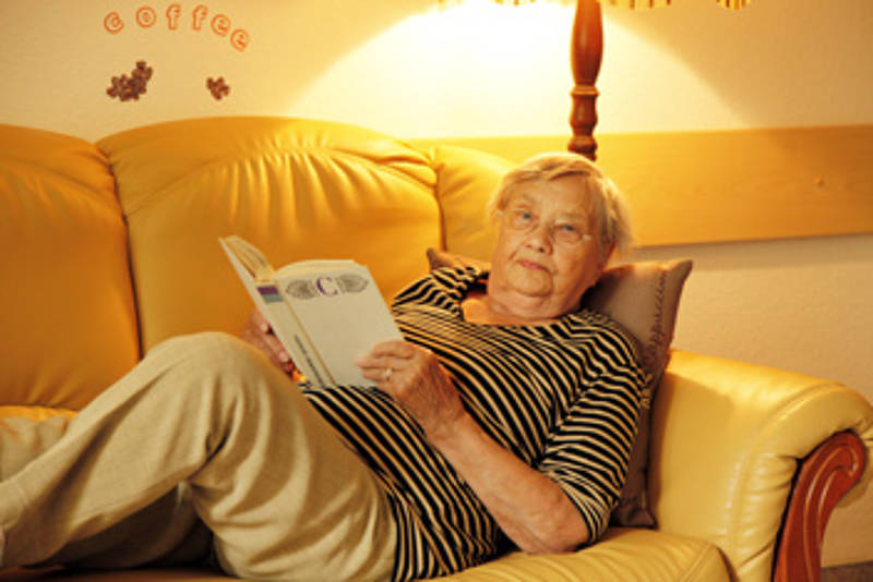 Seniorin liegt mit einem Buch auf dem Sofa